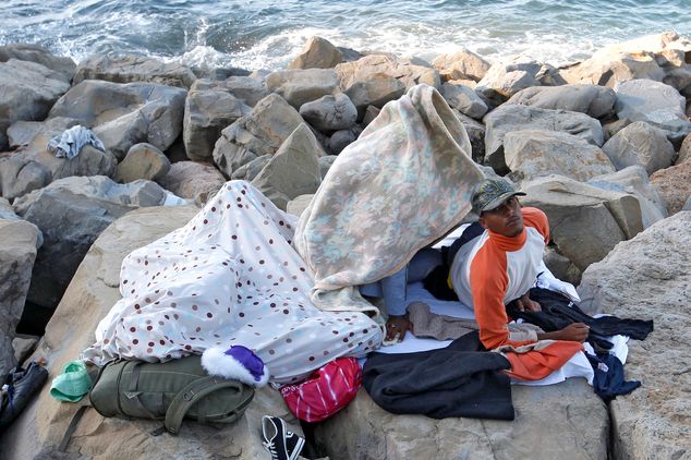 A migrant wakes up as he sleeps with others on the rocky beach at the France's Mediterranean border with Italy near Menton, southeastern France, Monday, June 15, 2015. French border police blocked border crossings last week, citing the influx of migrants, and about 200 would-be refugees have refused to leave the rocks of Ventimiglia, Italy, just a few kilometers from the swank resorts of Nice and Saint-Jean-Cap-Ferrat on the French Riviera. (AP Photo/Lionel Cironneau)