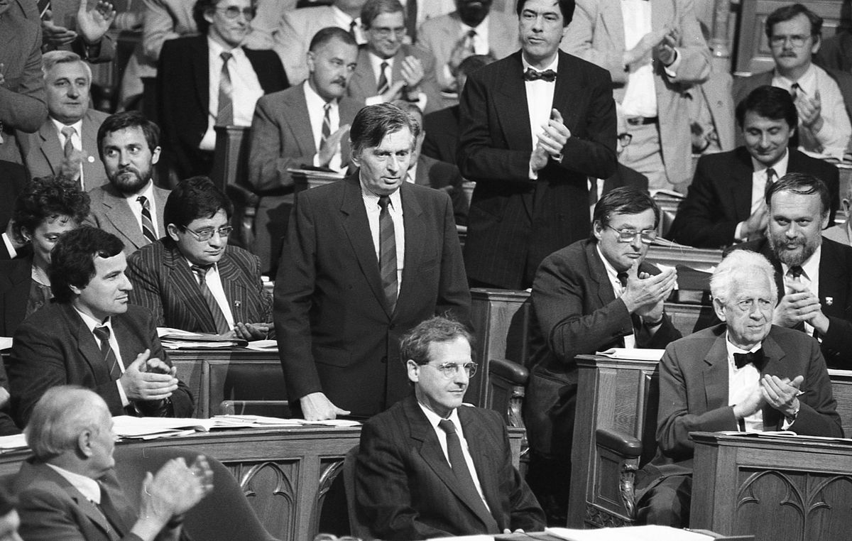 Médiaháború (5. rész)1990. Parlament, az Országgyűlés ülése. Előtérben Göncz Árpád, Sólyom László, Szentágothai János. Középen áll Antall József miniszterelnök, tőle jobbra Balsai István és Salamon László, mögöttük állva tapsol Csóti György, tőle balra Antall József mögött Zétényi Zsolt. A jobb felső sarokban Zacsek Gyula / Forrás: Fortepan.hu, adományozó: SZALAY ZOLTÁN
