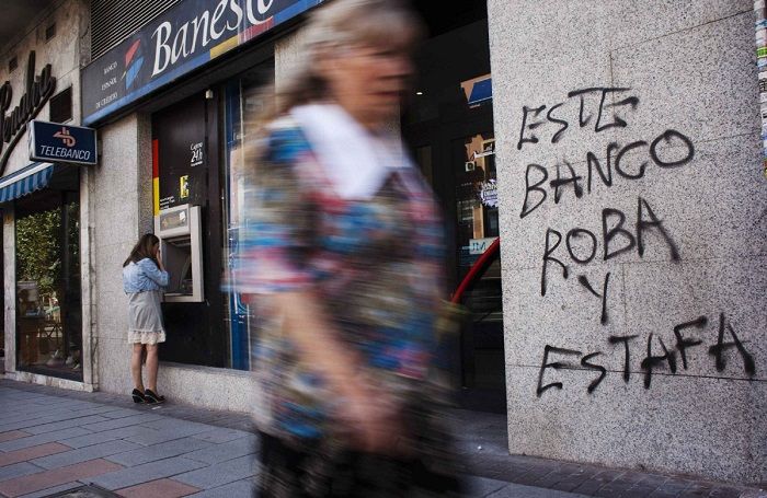 A spanyolok elégedetlenek, és egyre többen nem kérnek a trojkából, a bankokból. A képen egy spanyol pénzintézet látható, rajta pedig a felirat: